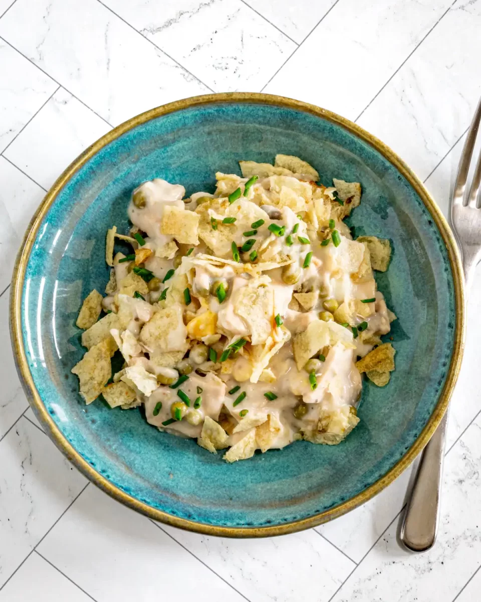 Creamy potato salad with peas and chopped chives on blue ceramic plate.