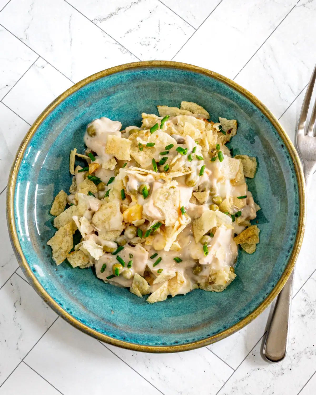 Creamy potato salad with peas and chopped chives on blue ceramic plate.