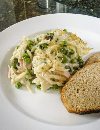 tuna casserole with orzo, peas, and cheese on a plate with sliced bread