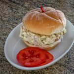a turkey and egg salad sandwich on a plate with sliced tomatoes on the side