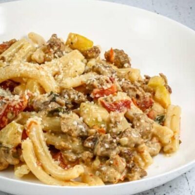 tuscan pasta in a bowl with italian sausage, sun dried tomatoes, and zucchini