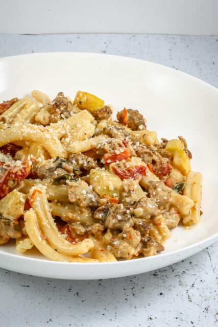 tuscan pasta in a bowl with italian sausage, sun dried tomatoes, and zucchini