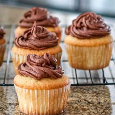 moist vanilla cupcakes on a rack with chocolate frosting