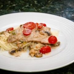 veal marsala with cream sauce on a plate with angel hair pasta.