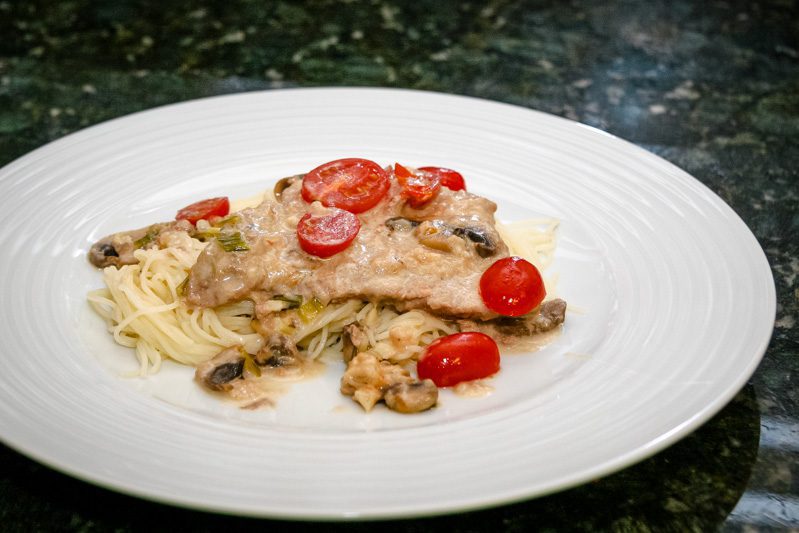 veal marsala with cream sauce on a plate with angel hair pasta.