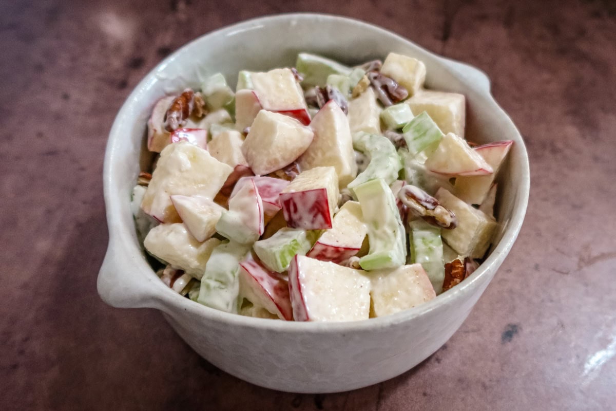 A bowl of waldorf salad with apples, pecans, raisins, and a mayonnaise dressing.