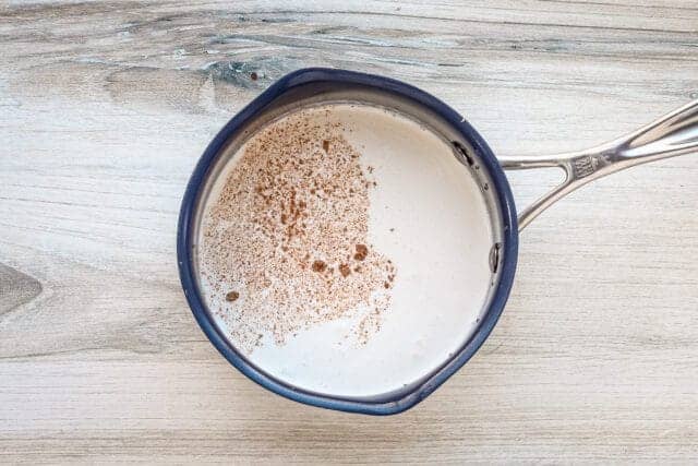 Creamy milk with cinnamon sprinkled on top in a small blue saucepan.