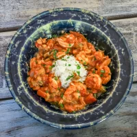 Steamed shrimp and vegetable stew with rice in a dark bowl on a wooden table.