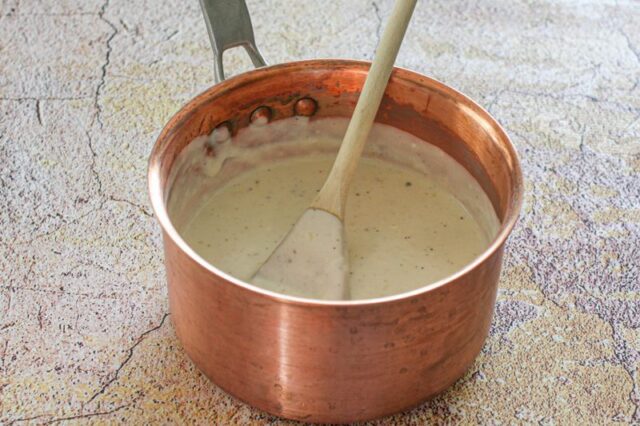 basic white sauce in a copper saucepan with wooden spoon