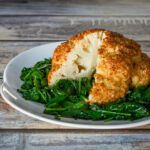 whole roasted cauliflower on a bed of steamed spinach