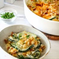 Zucchini casserole on a plate with the baking dish in the background.